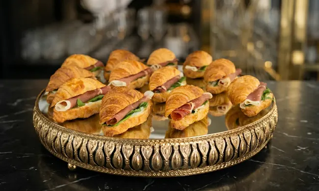 Croissants de jamón serrano y rúcula en bandeja dorada para catering y cóctel premium en Santiago.