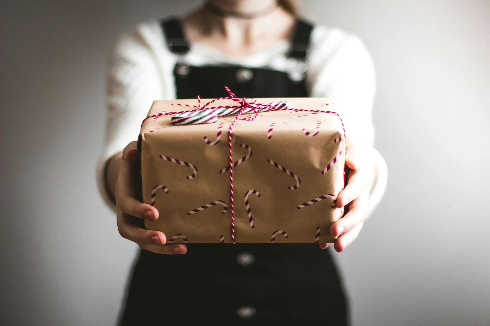 Woman in black apron holding kraft paper gift box with red and white twine bow and candy cane pattern.