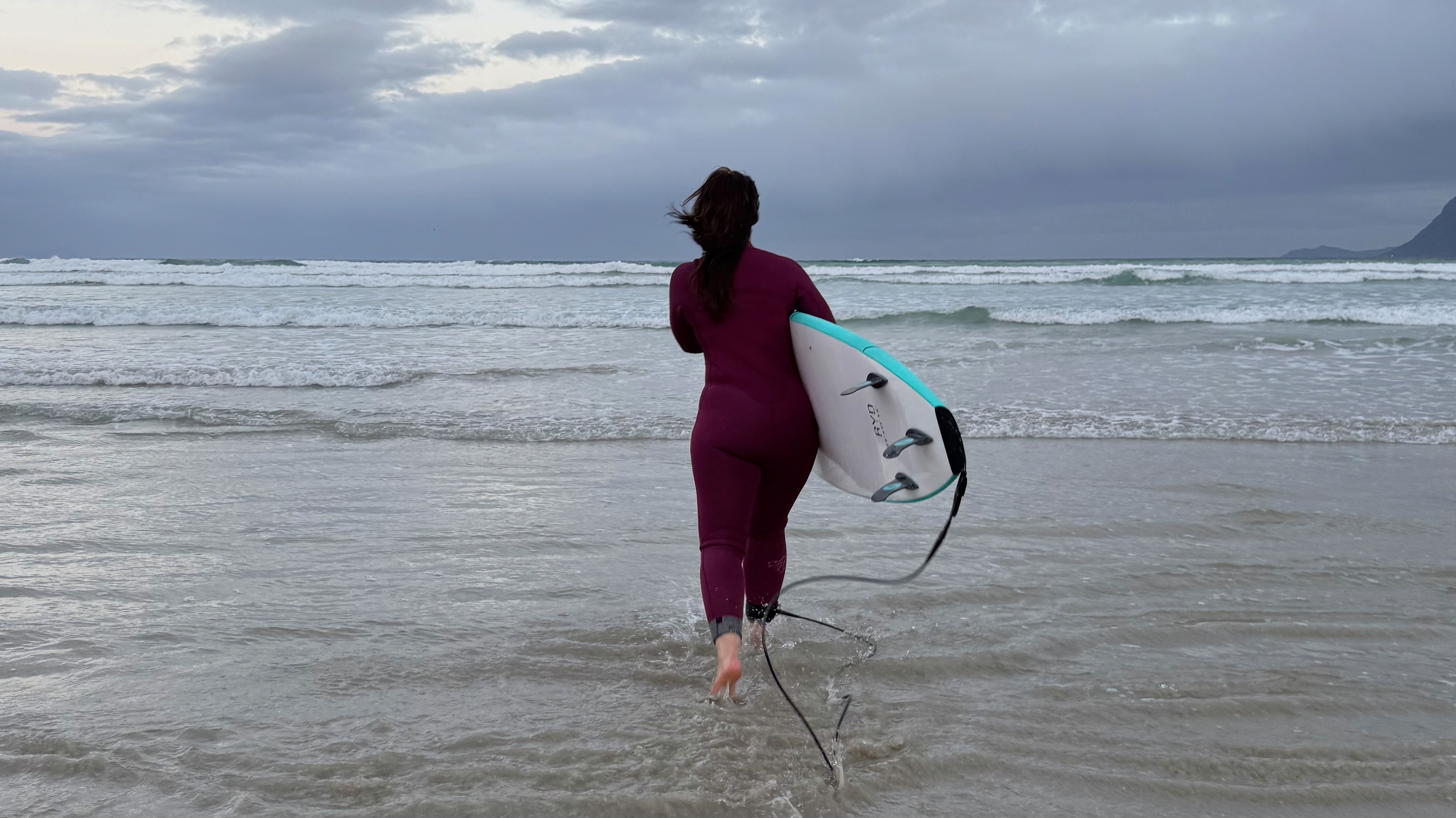 Female surfer going into the ocean at Muizenberg beach in Cape Town, holding her surfboard
