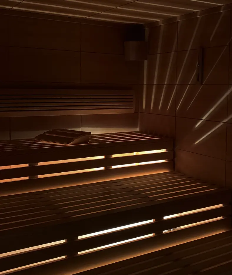 A warmly lit, wooden sauna interior with tiered seating, creating a serene and relaxing atmosphere.
