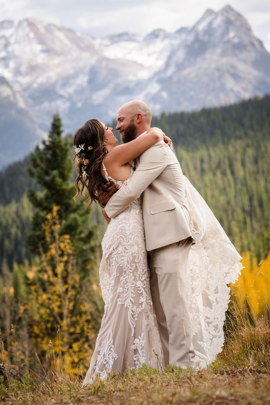 The groom lifts and swirls the bride during their portrait session, her lace veil caught in the breeze. The golden fall foliage provides a vibrant pop of color against the alpine scenery.