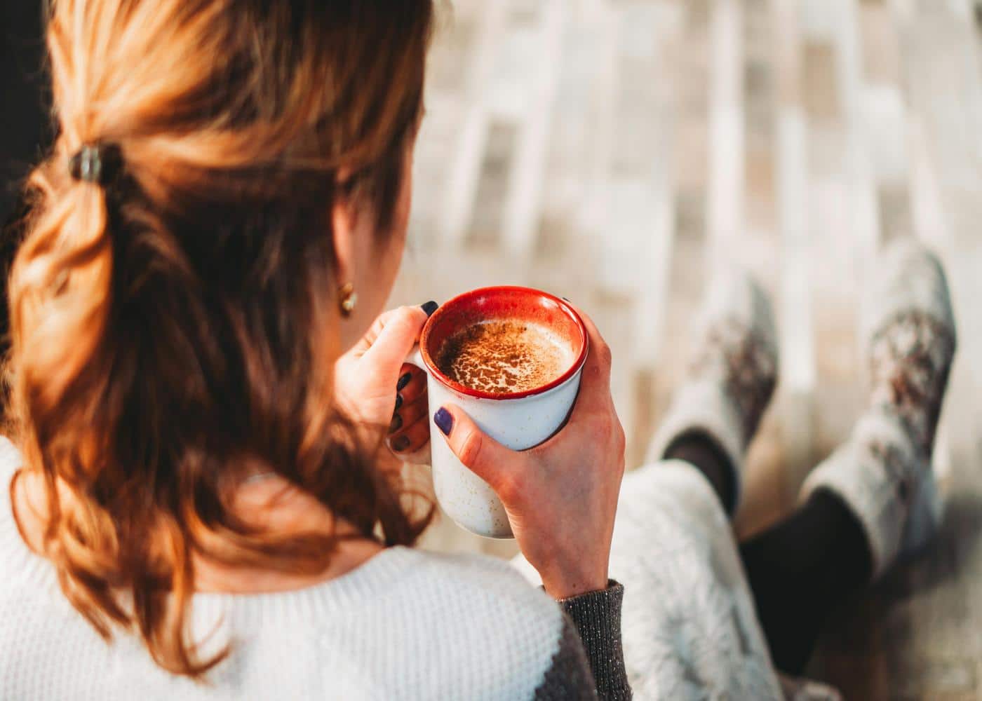 Back of a woman shown holding a cup of coffee