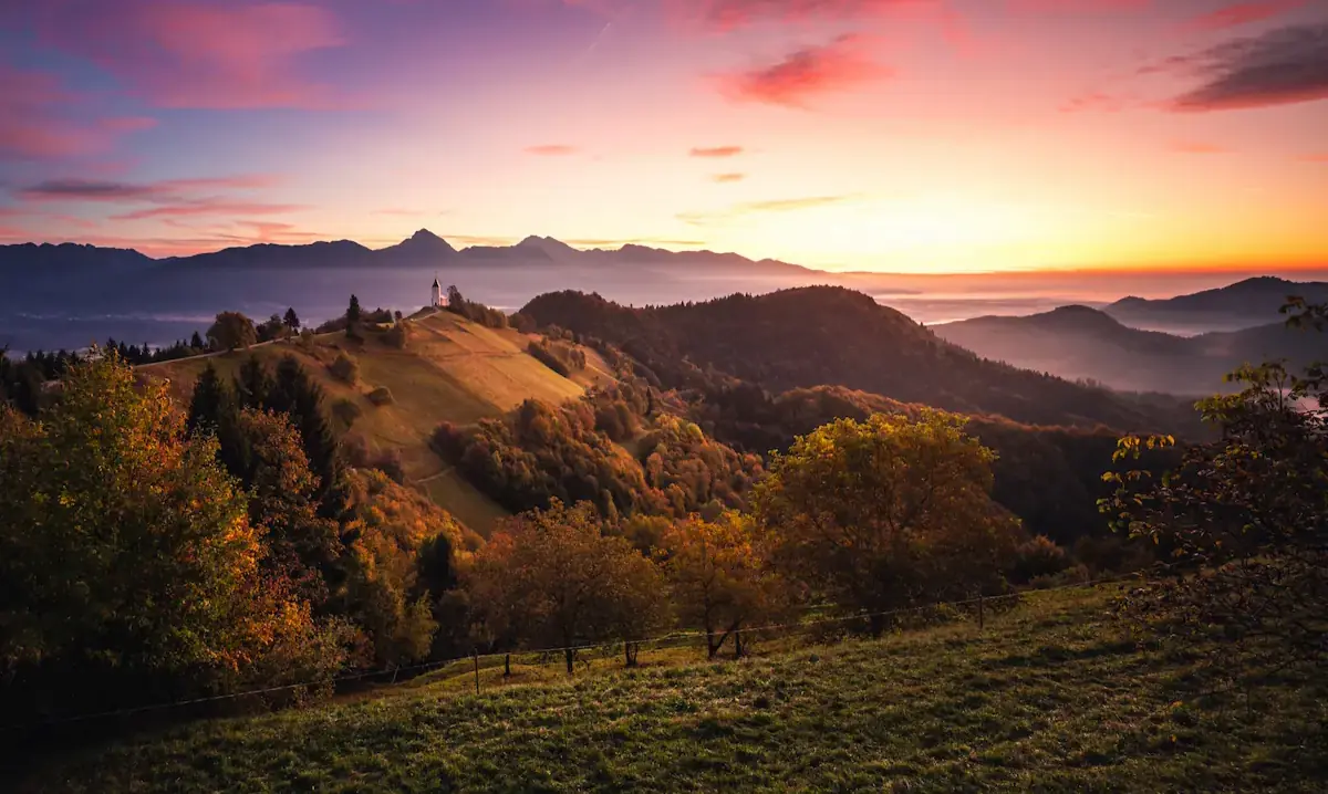 A stunning sunset over rolling hills at Jamnik, Slovenia, with vibrant clouds and warm light illuminating the landscape.