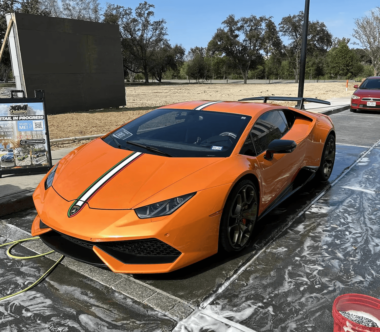 An orange Lamborghini Huracán with Italian flag stripes undergoing a professional hand wash and foam bath at a Houston mobile detailing station.