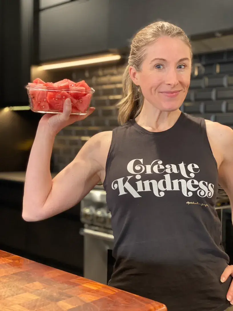 Heather Hausman in a kitchen holds a glass container filled with watermelon cubes.