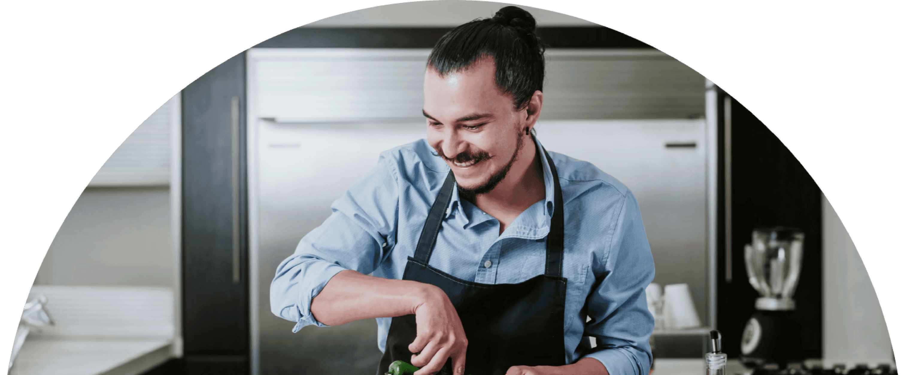 Man in an apron smiles while grinding ingredients in a kitchen