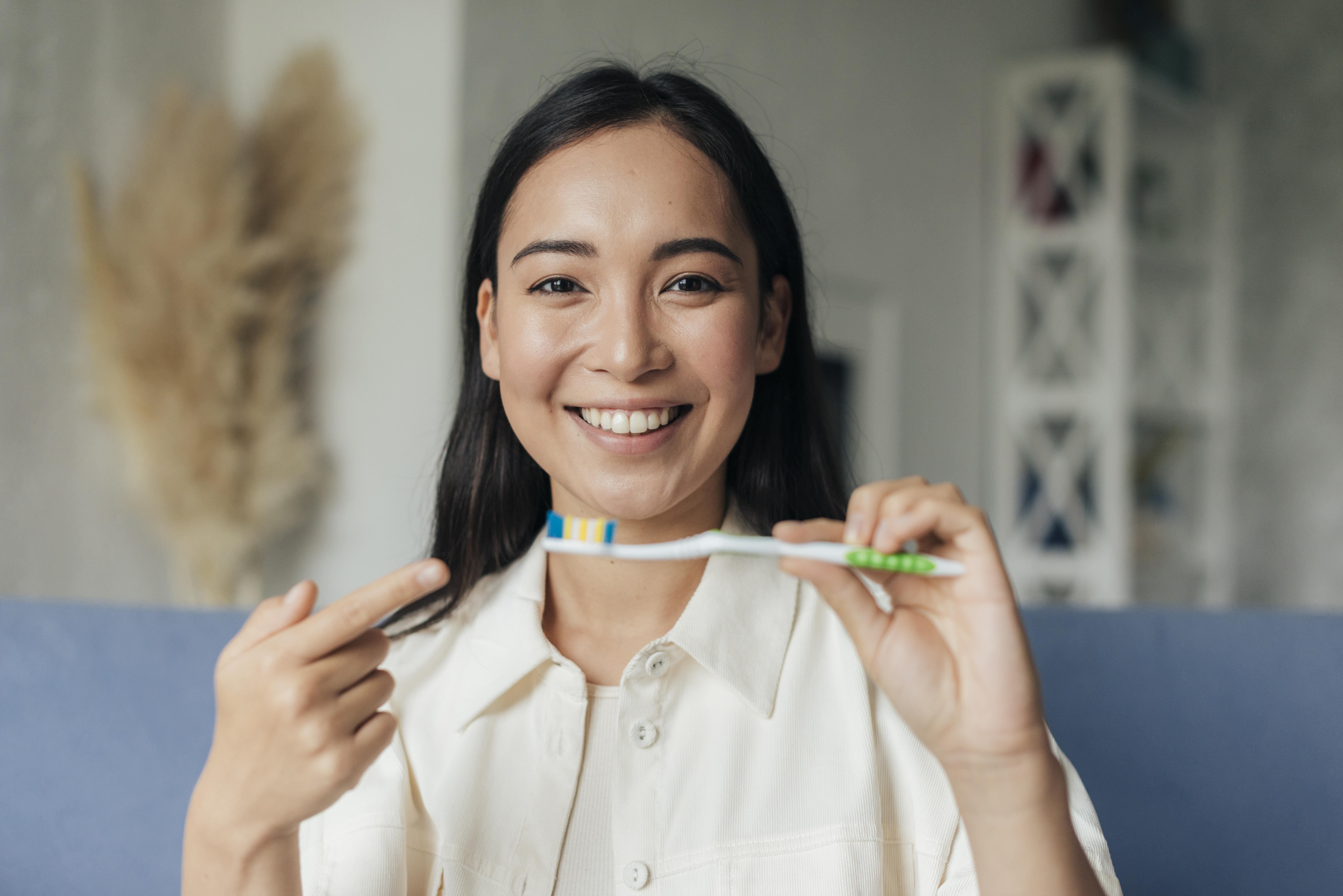 A smiling woman holding a toothbrush and pointing at it, promoting dental hygiene