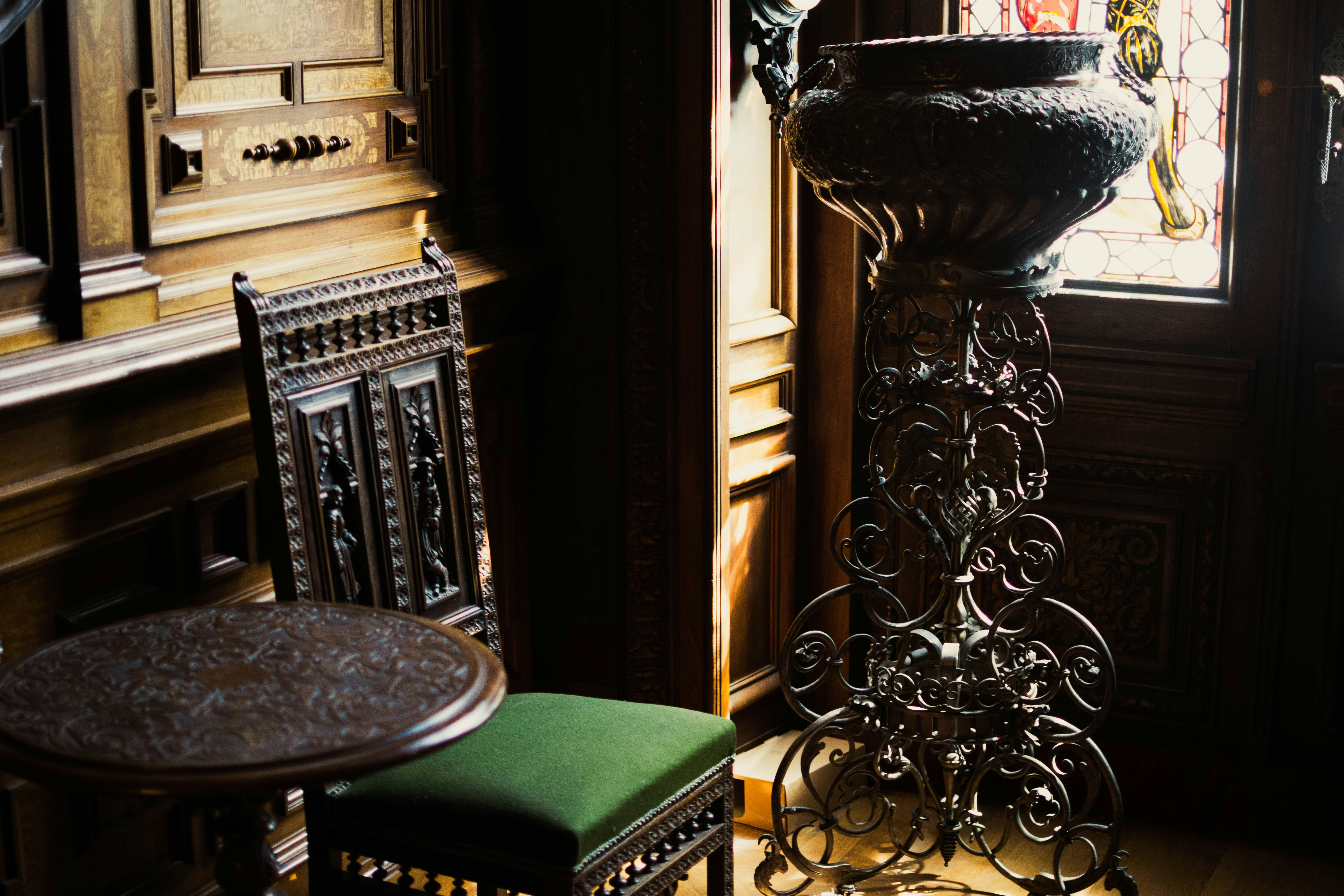 A traditional chair and table with a pot on a stand, illuminated by window light.