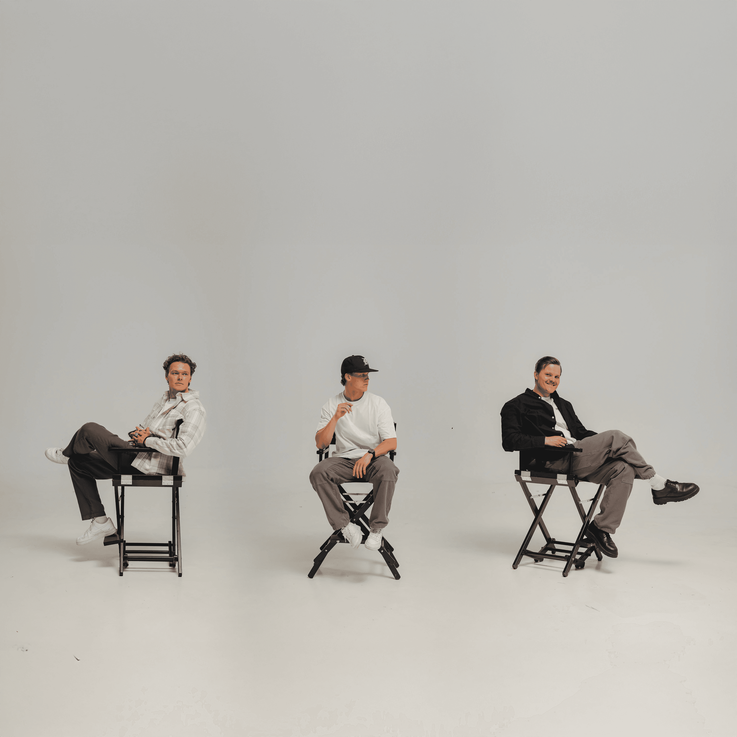 Kolme henkilöä istuu studiotuoleilla vaaleassa studiossa rivissä.