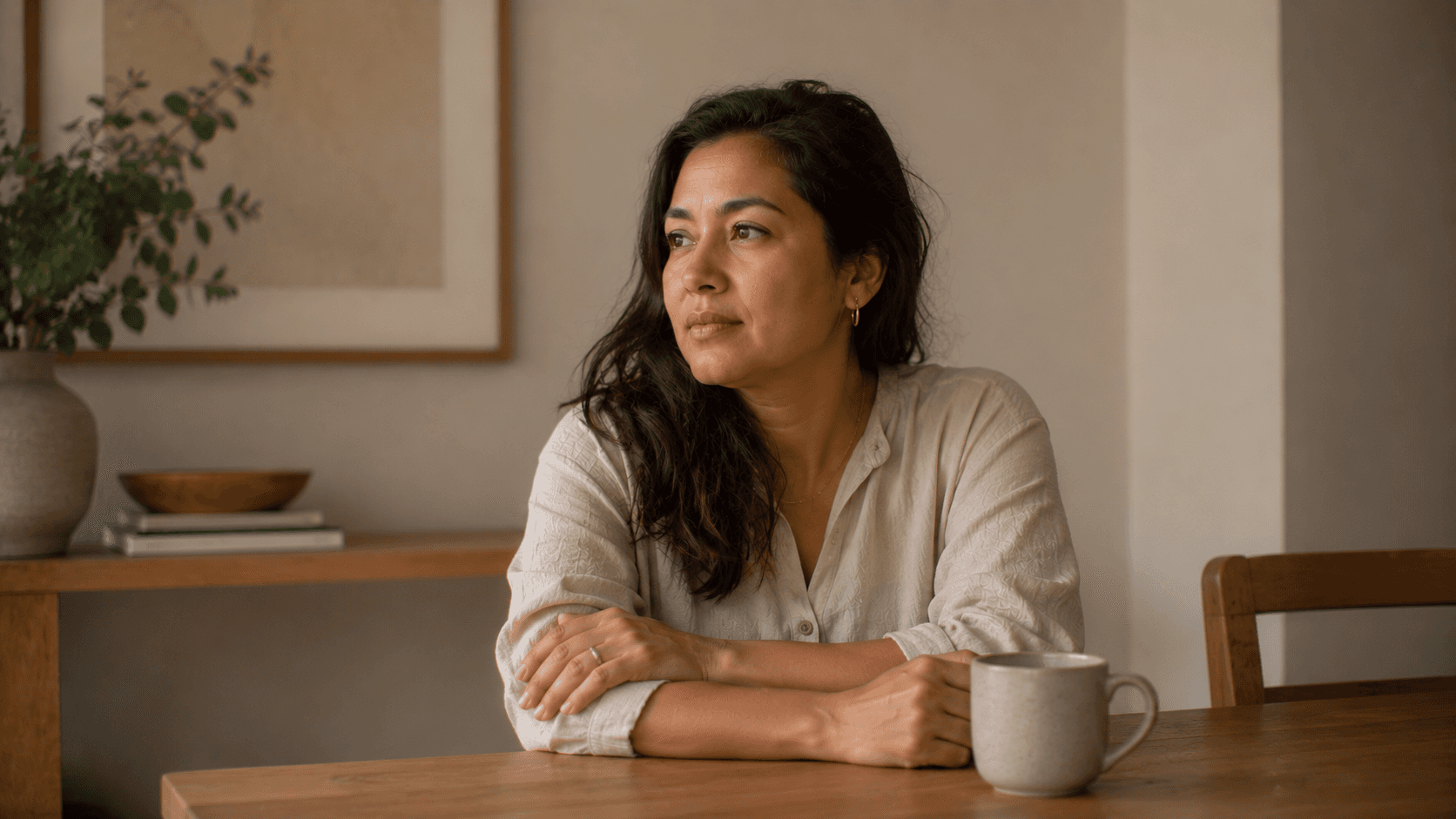 Woman sitting alone at a dining table in a softly lit modern home