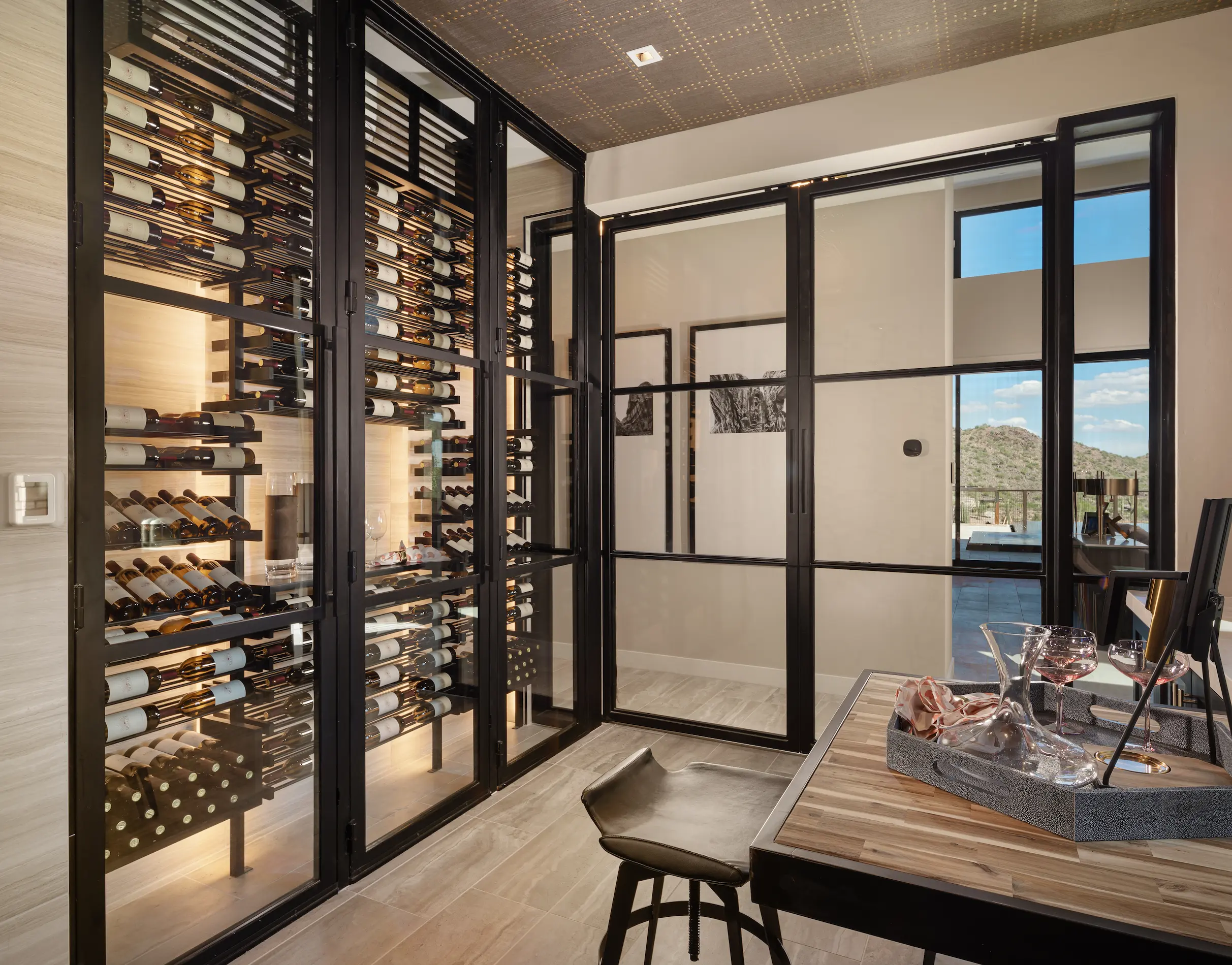 Modern glass-enclosed wine wall with black anodized metal racking and walnut shelving in a luxury dining room — custom wine cellar design by Innovative Wine Cellar Designs.