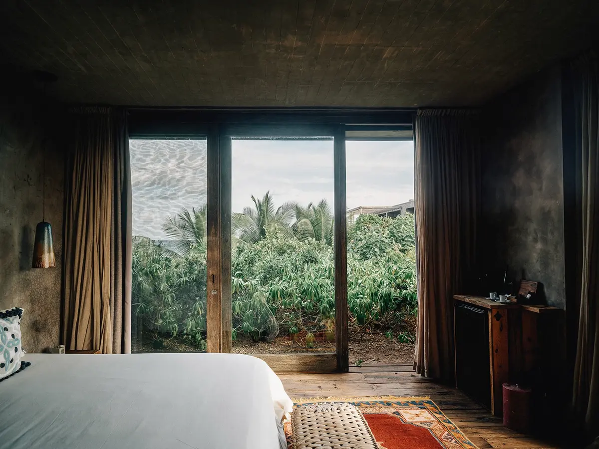 Aire Suite at Nômade Tulum featuring luxurious finishes and incredible design, comfortable bed with pillows and cushions, 2 hanging lamps in harmony, and huge window with jungle view.