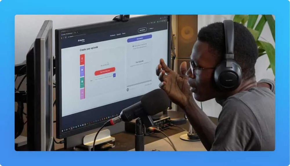 Man with headphones and desk microphone facing two monitores while recording a podcast