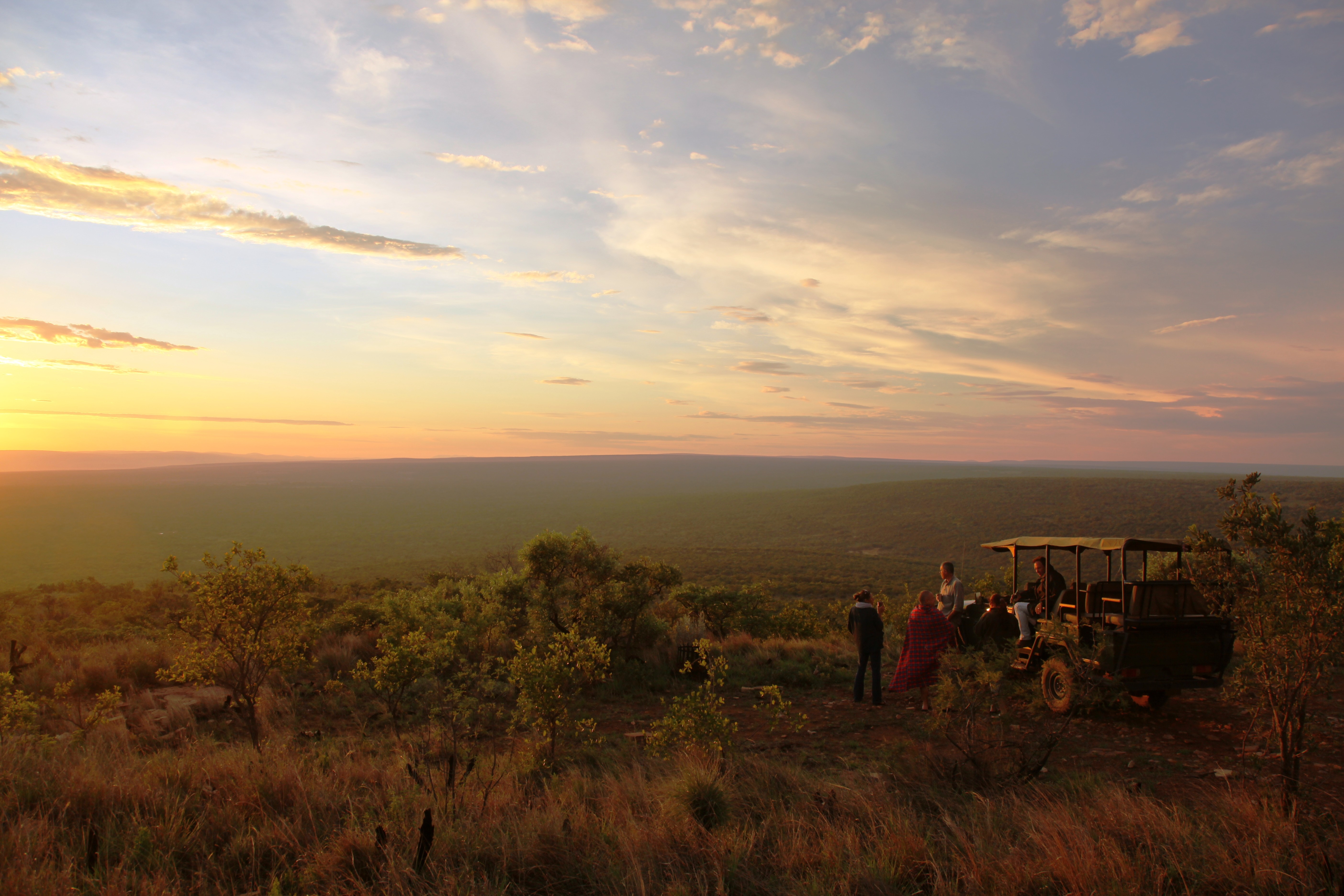 Grupp av ryttare på ridresa i Afrika galopperar över Serengetis vidsträckta slätter medan damm och gnuhjordar rör sig över horisonten under the great migration.