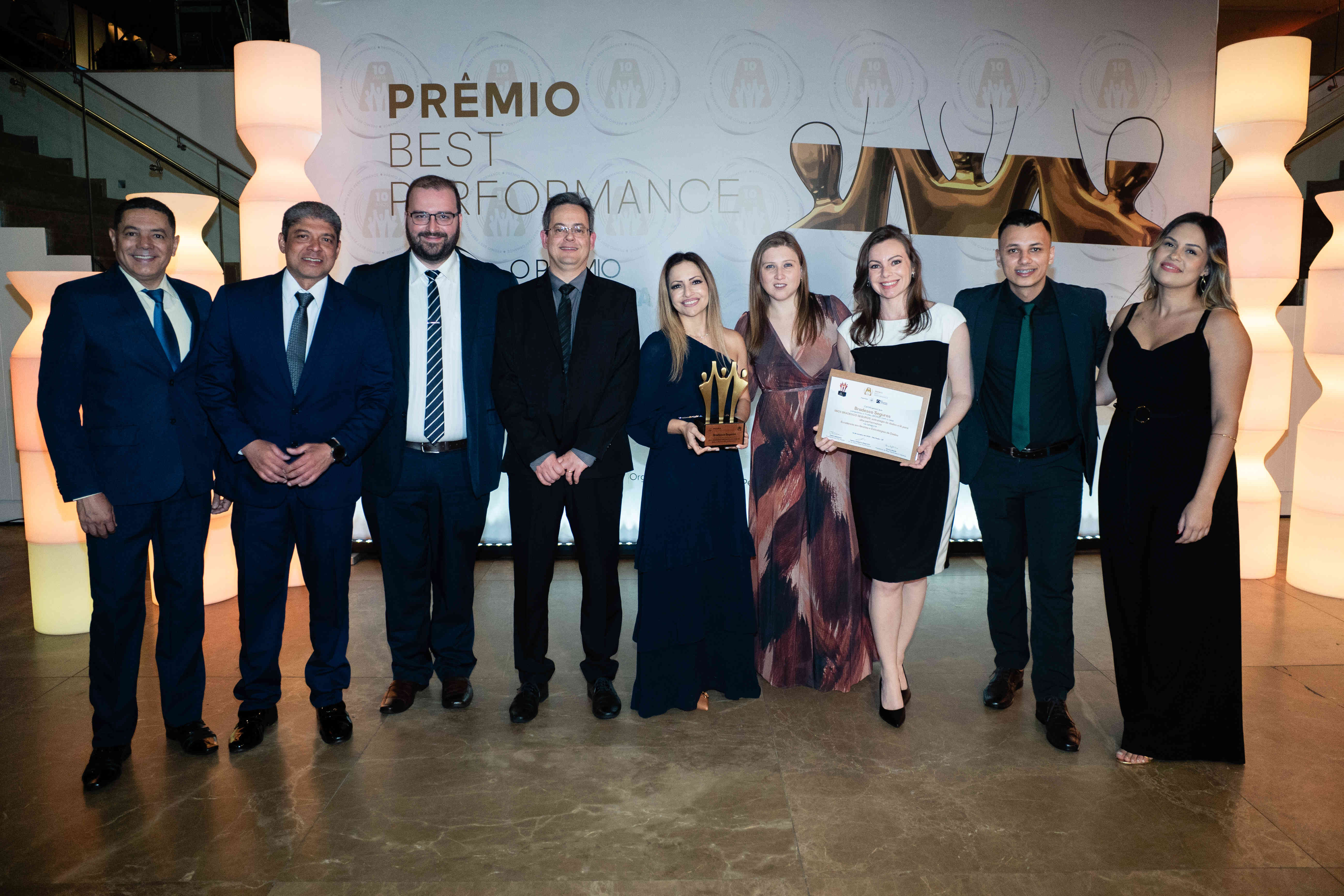 Executivos da Bradesco Seguros posando com troféu bronze e certificado no palco do Prêmio Best Performance 2025