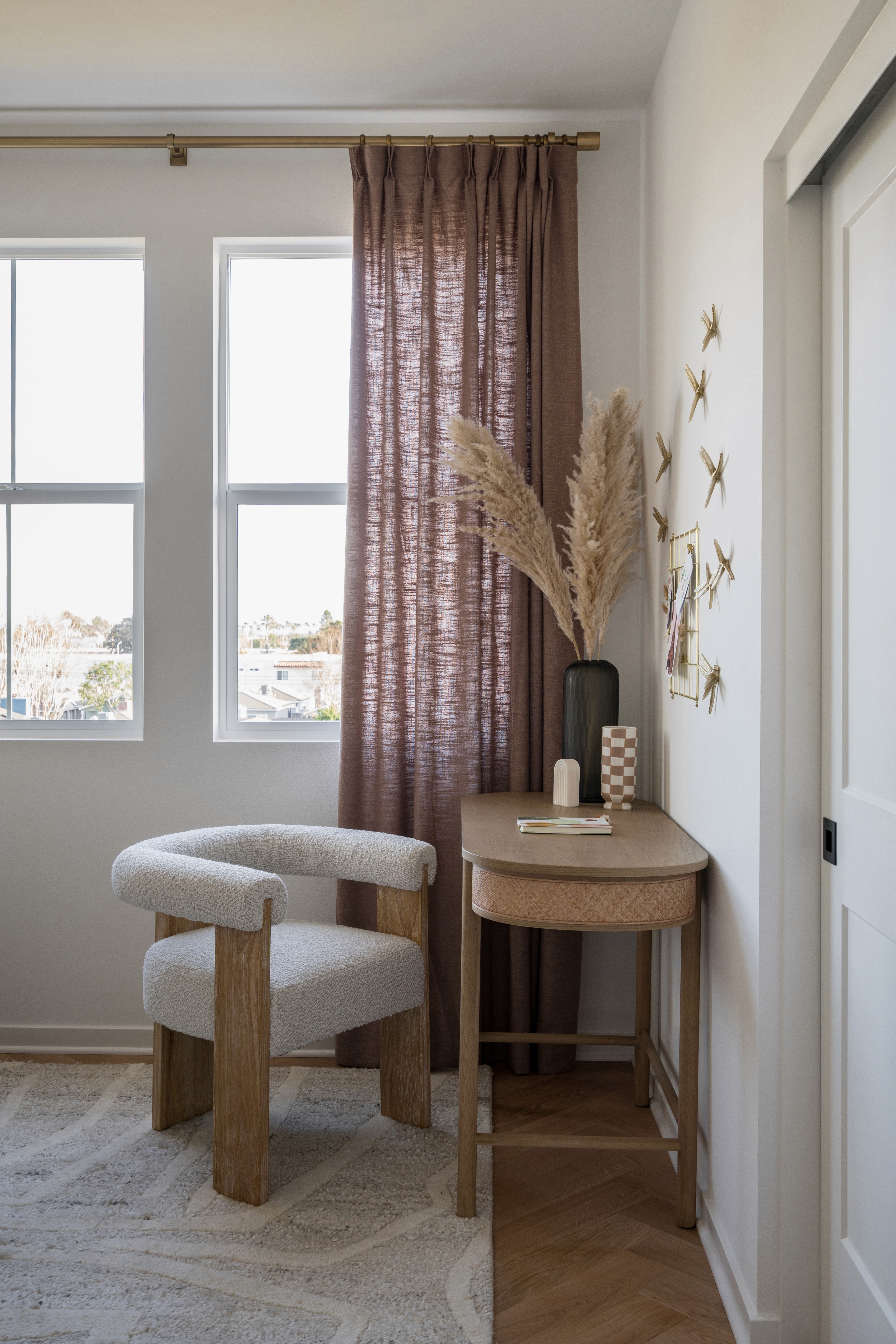 White, boucle desk chair and natural wood desk with dried flowers and burgundy floor to ceiling drapes and  patterned wall paper