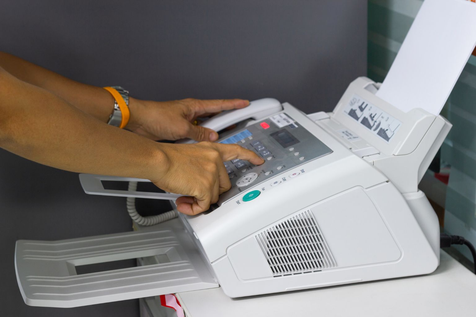 Hands operating a fax machine with paper loaded
