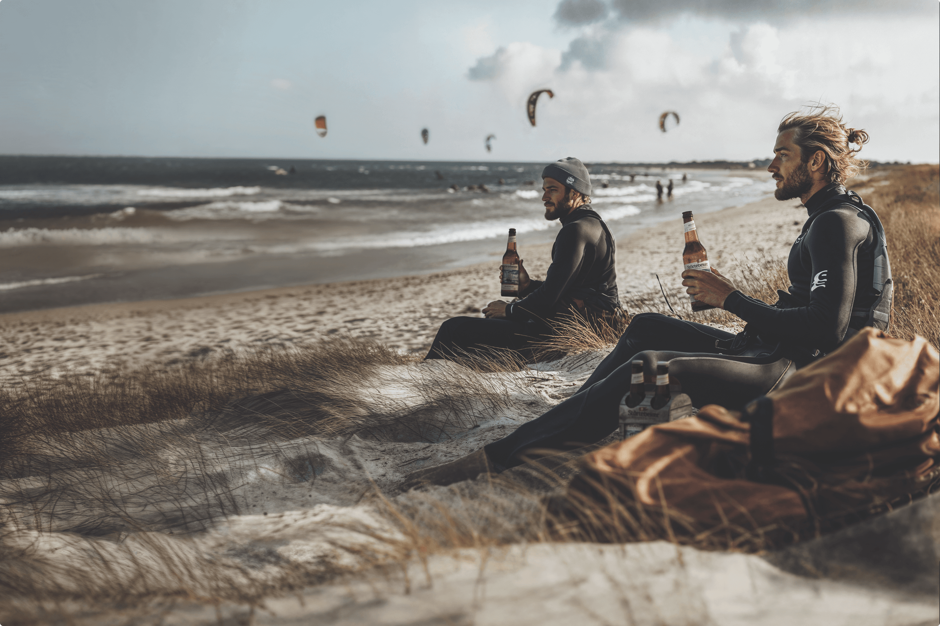 Two men in wetsuits on a beach with beer.