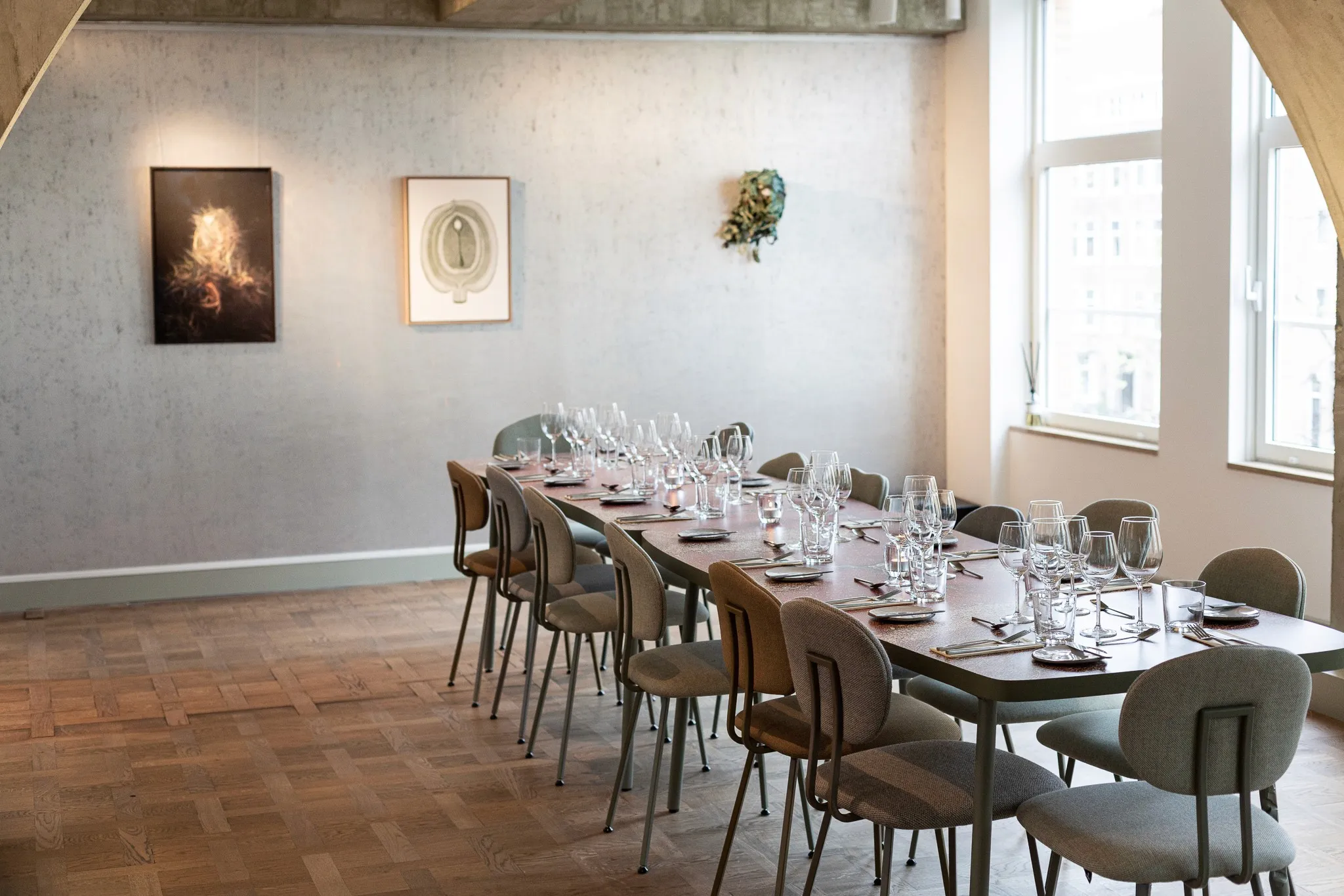 A spacious meeting room featuring a long table and artwork on white walls, with large windows letting in natural light.