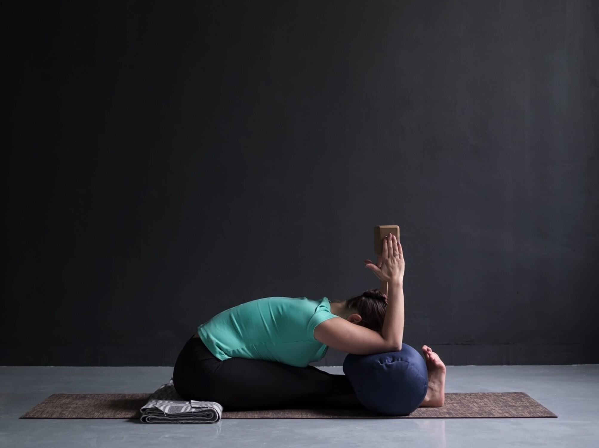 woman trying to lose weight doing yoga as a beginner and using a block and bolster to help with her seated forward fold