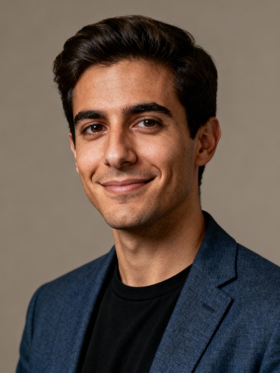 Smiling man in a blue blazer and black shirt against a neutral background. He appears confident and approachable, conveying a professional tone.