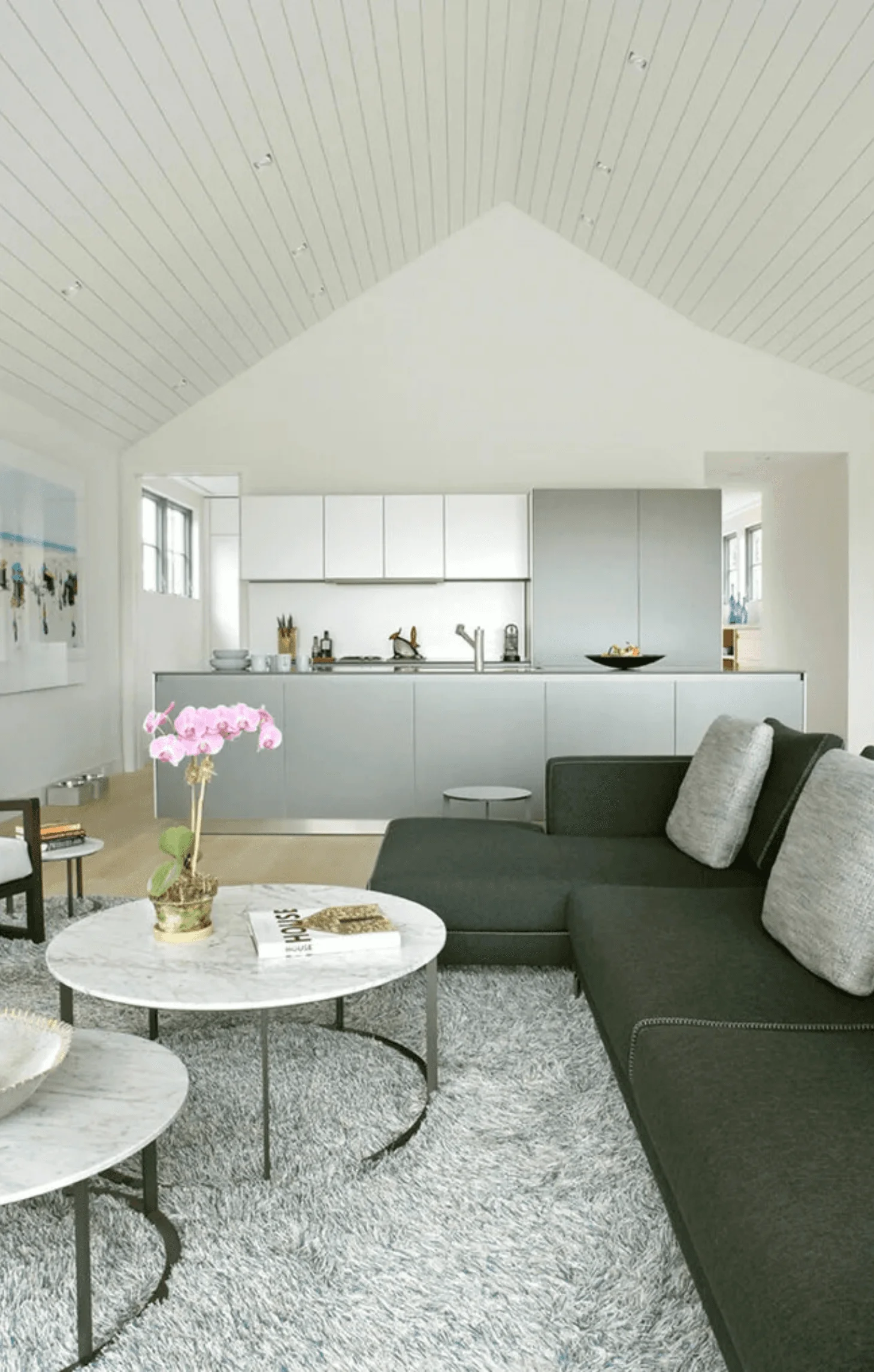 The living room's vaulted, wood-paneled ceiling rises above a gray sectional sofa and round marble coffee tables