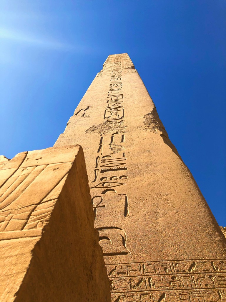 A towering ancient Egyptian obelisk adorned with intricate hieroglyphics stands majestically under a bright blue sky, symbolizing the rich historical legacy and architectural prowess of ancient Egypt.