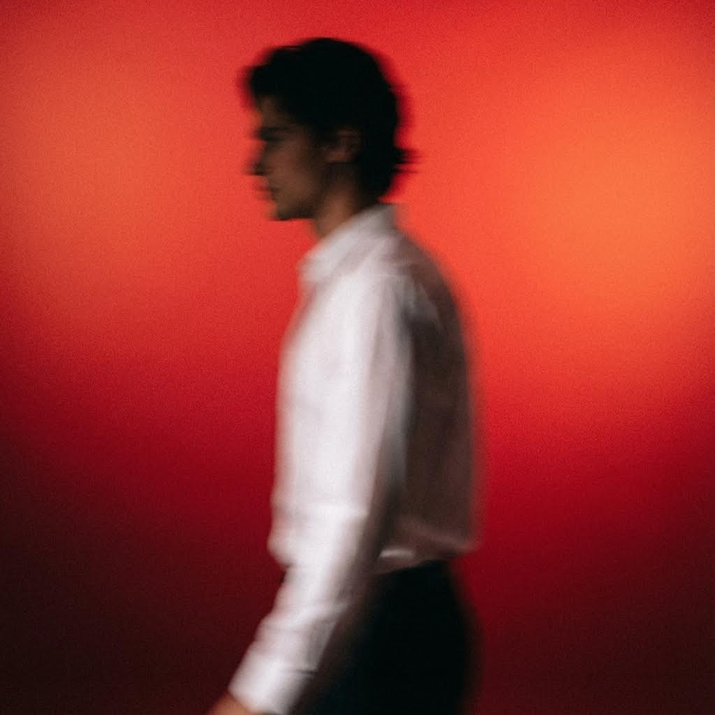 Upclose panning shot of a blurry man walking across wearing a white shirt silhouette, soft focus, film grain, against a red gradient background, motion blur.