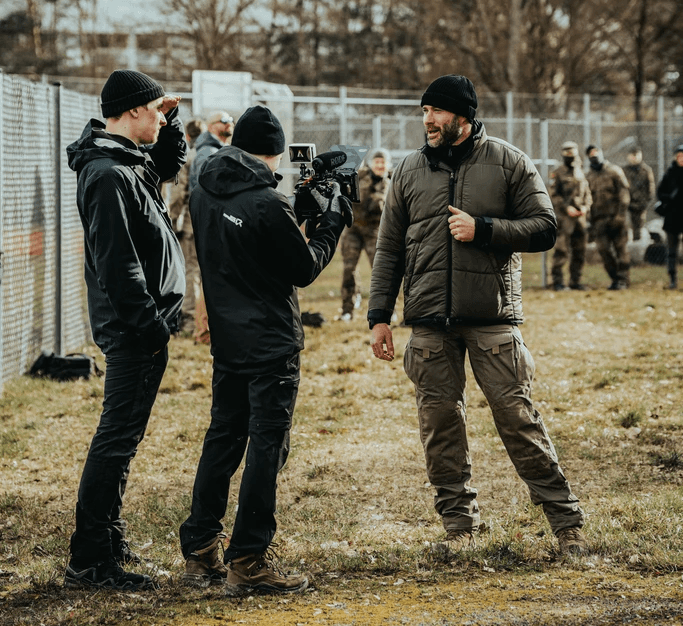 A close-up of a person wearing green-tinted glasses, with a serious expression and smooth skin.