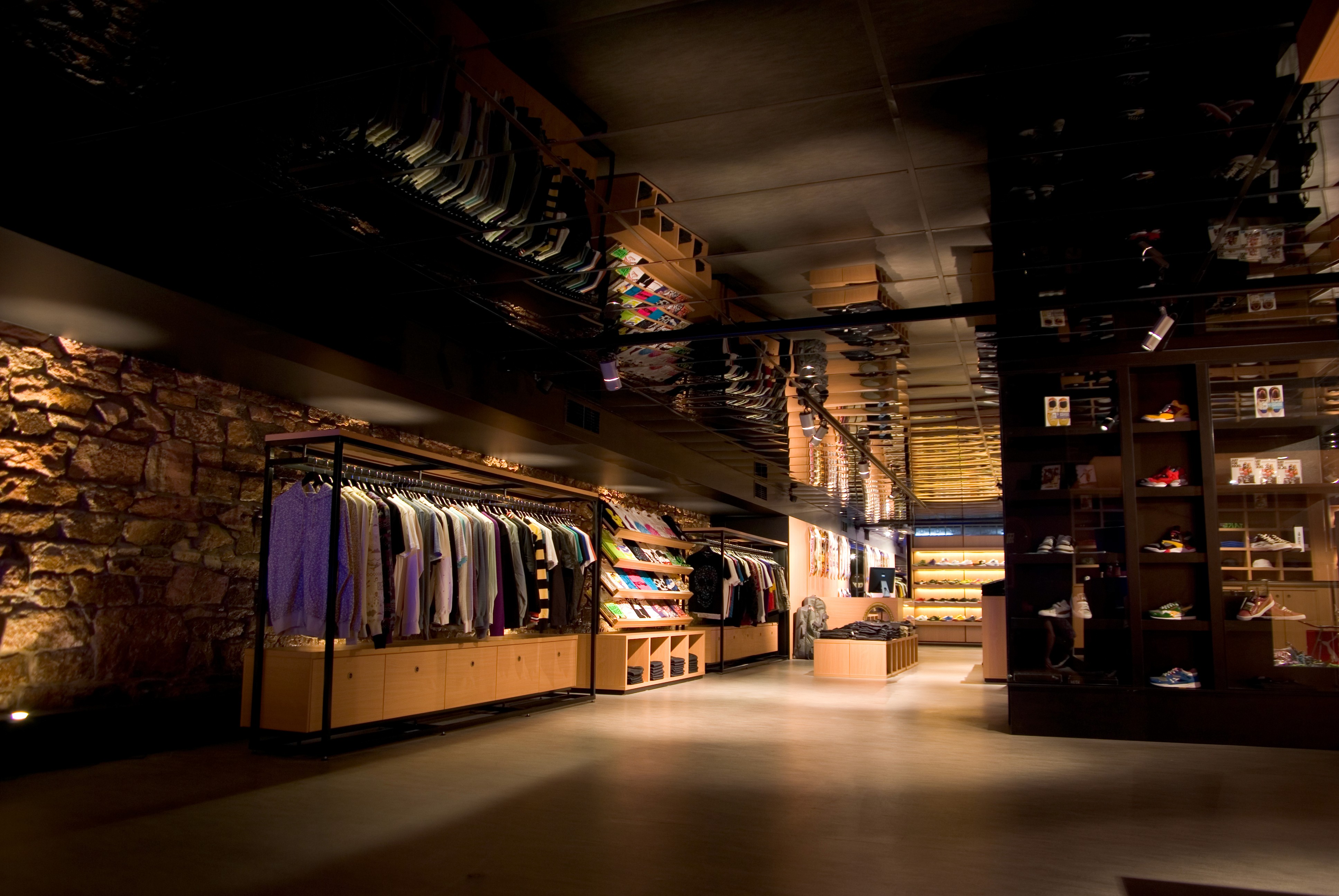 Long view through Apartment Store retail space with clothing racks, stone wall detail, and low ambient lighting.