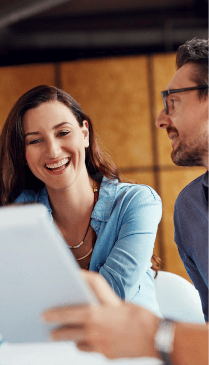 A man and woman smile together while viewing a tablet, sharing a moment of joy and connection.