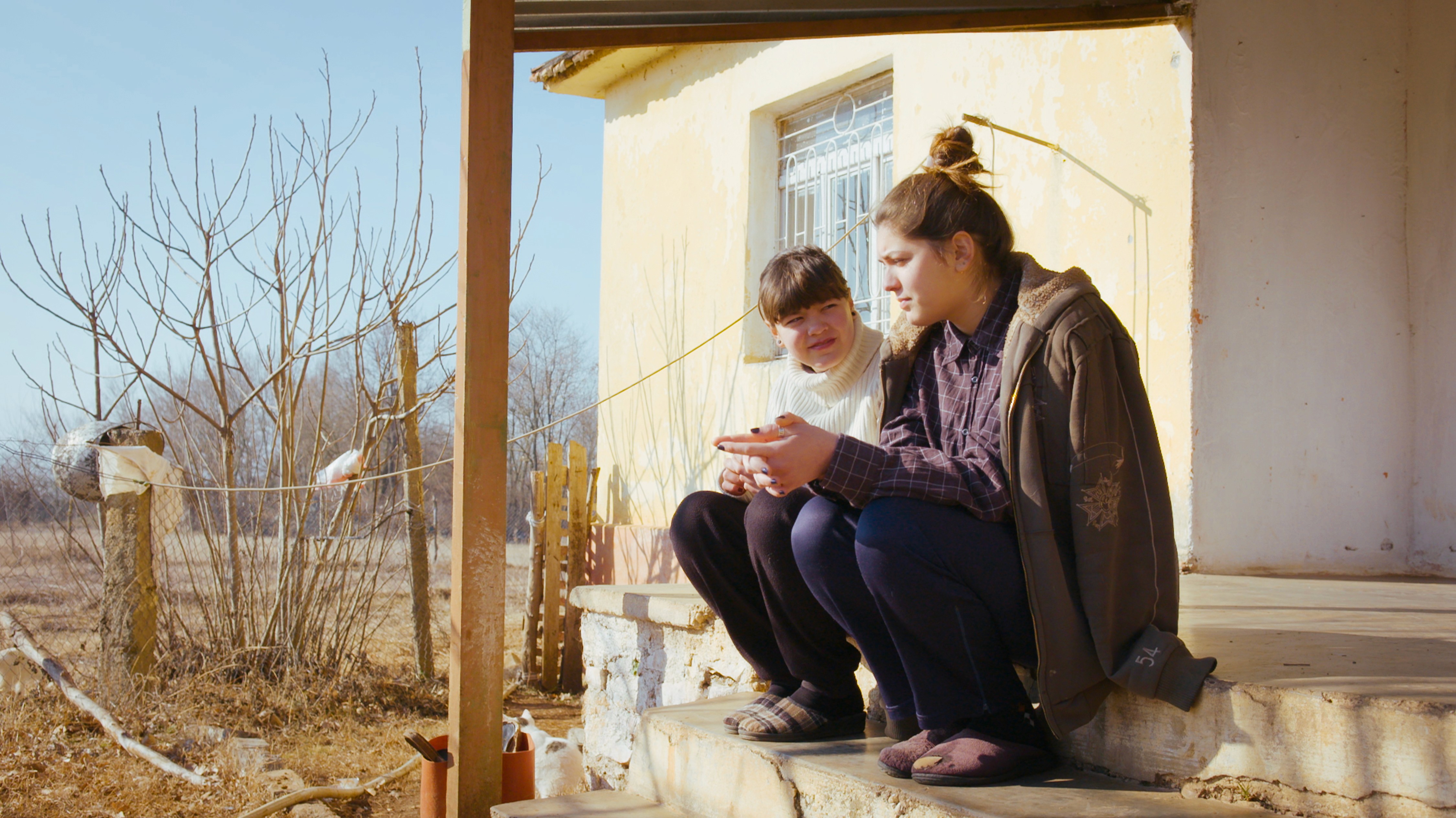 A woman in a light green suit sitting before a large circular opening that overlooks a calm, deep blue ocean.