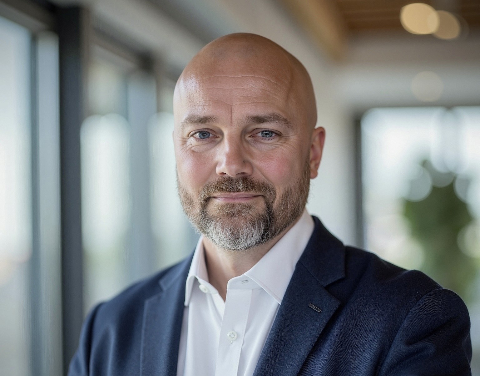 Smiling woman with glasses working on a laptop at a wooden desk, with a pink coffee mug beside her