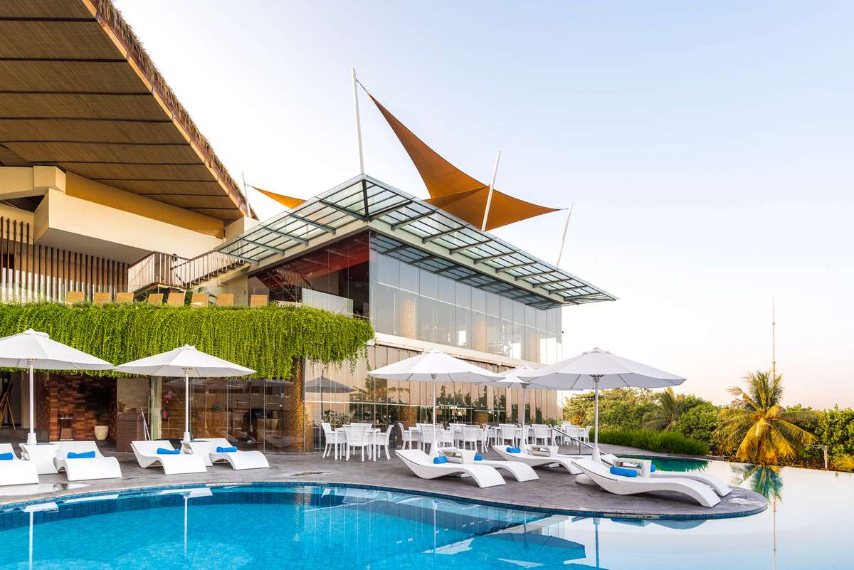 A modern poolside lounge with white umbrellas and blue cushions overlooks a swimming pool under bright daylight.