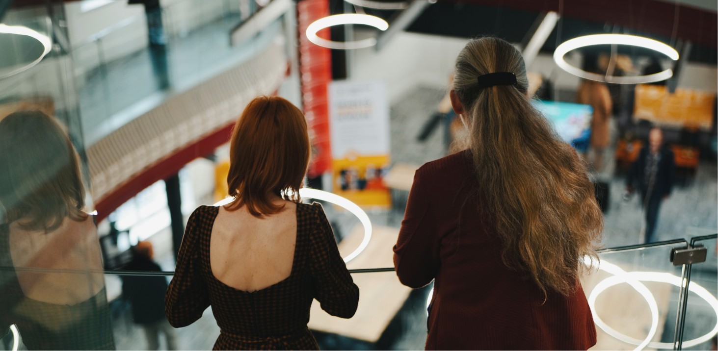 Two people standing and sitting at a train station.