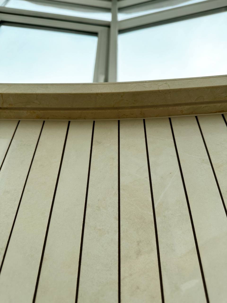 Radius wall under a curved window sill, tiled in strips cut from large-format porcelain offcuts