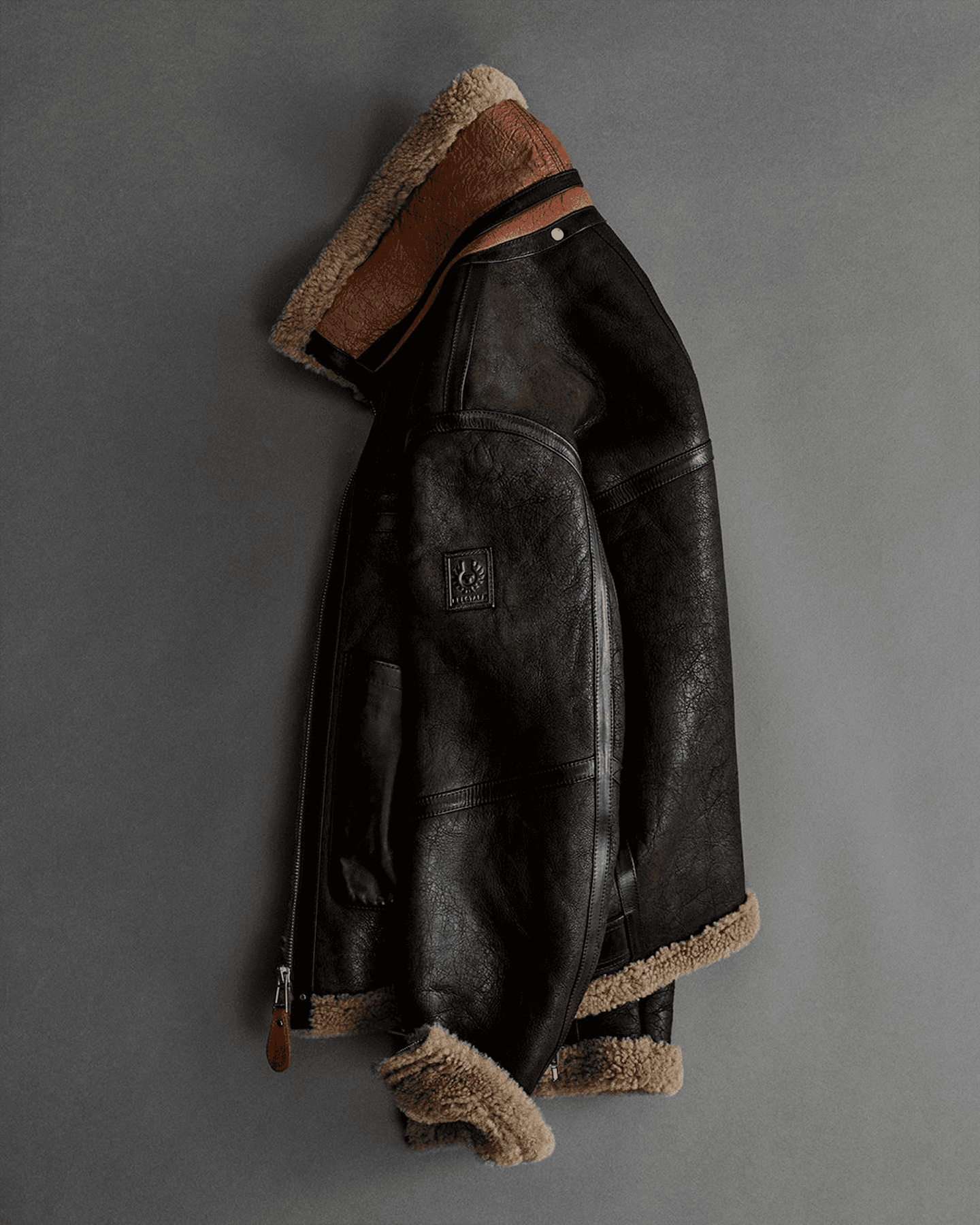Blouson aviateur en cuir et peau lainé, accroché à un mur gris