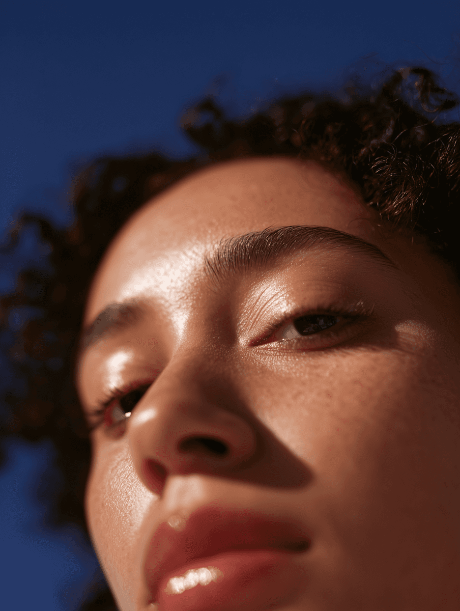 Low-angle close-up portrait of a woman with curly hair and freckles against a clear blue sky.