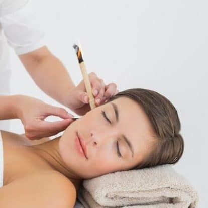 A woman lies relaxed on a treatment table, receiving a facial treatment with gentle care.