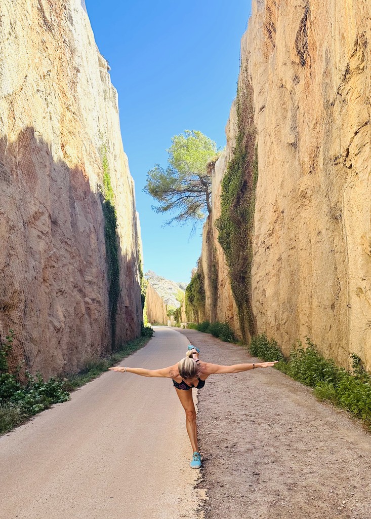 Silvia con los brazos y una pierna levantada, realizando postura de yoga en la vía verde de Benicasim