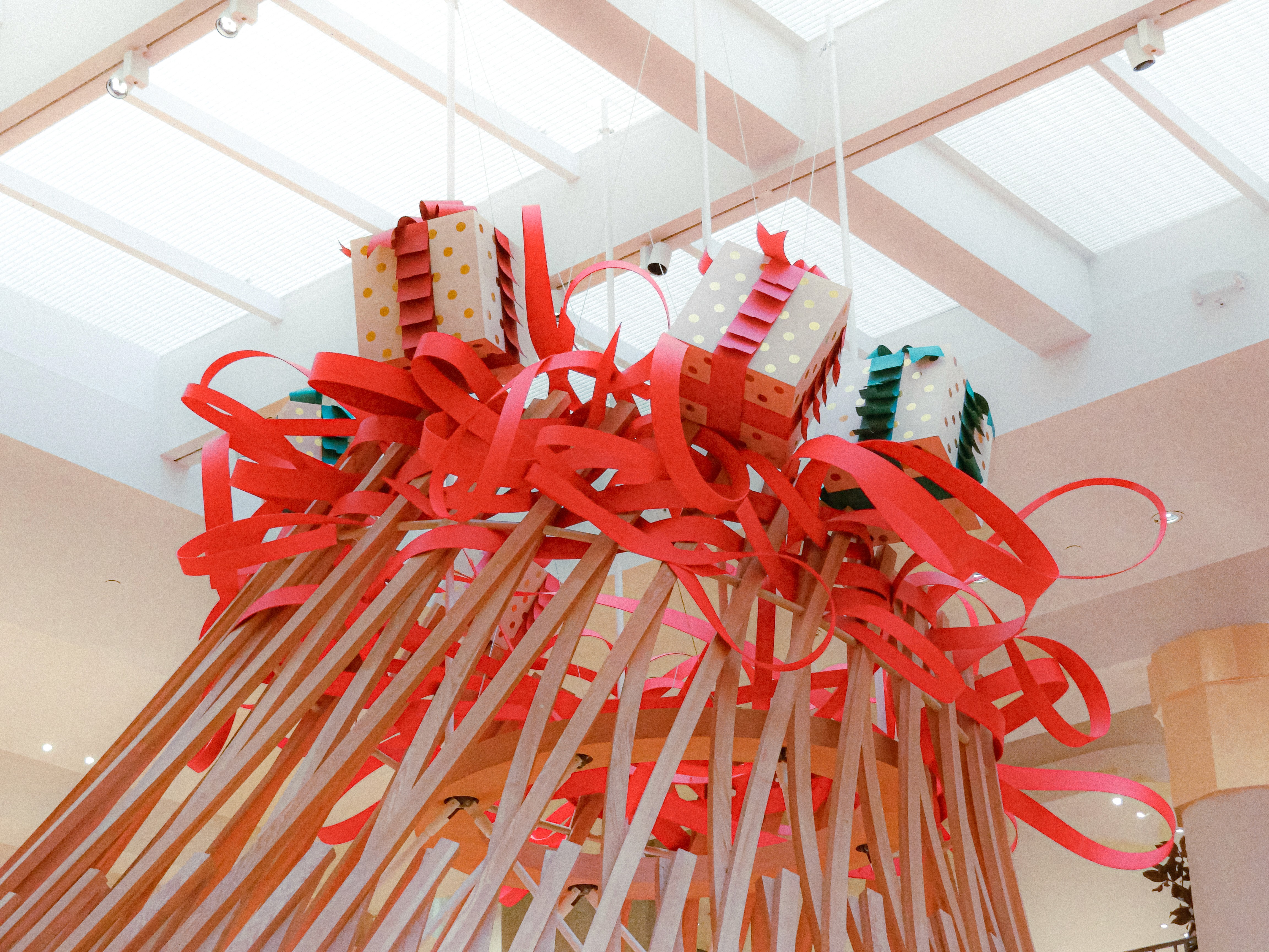 Detailed view of the Hermès holiday scenography featuring gold-dotted gift boxes suspended within a dynamic whirlwind of red ribbons and a light wooden architectural structure, designed by WM Paris.