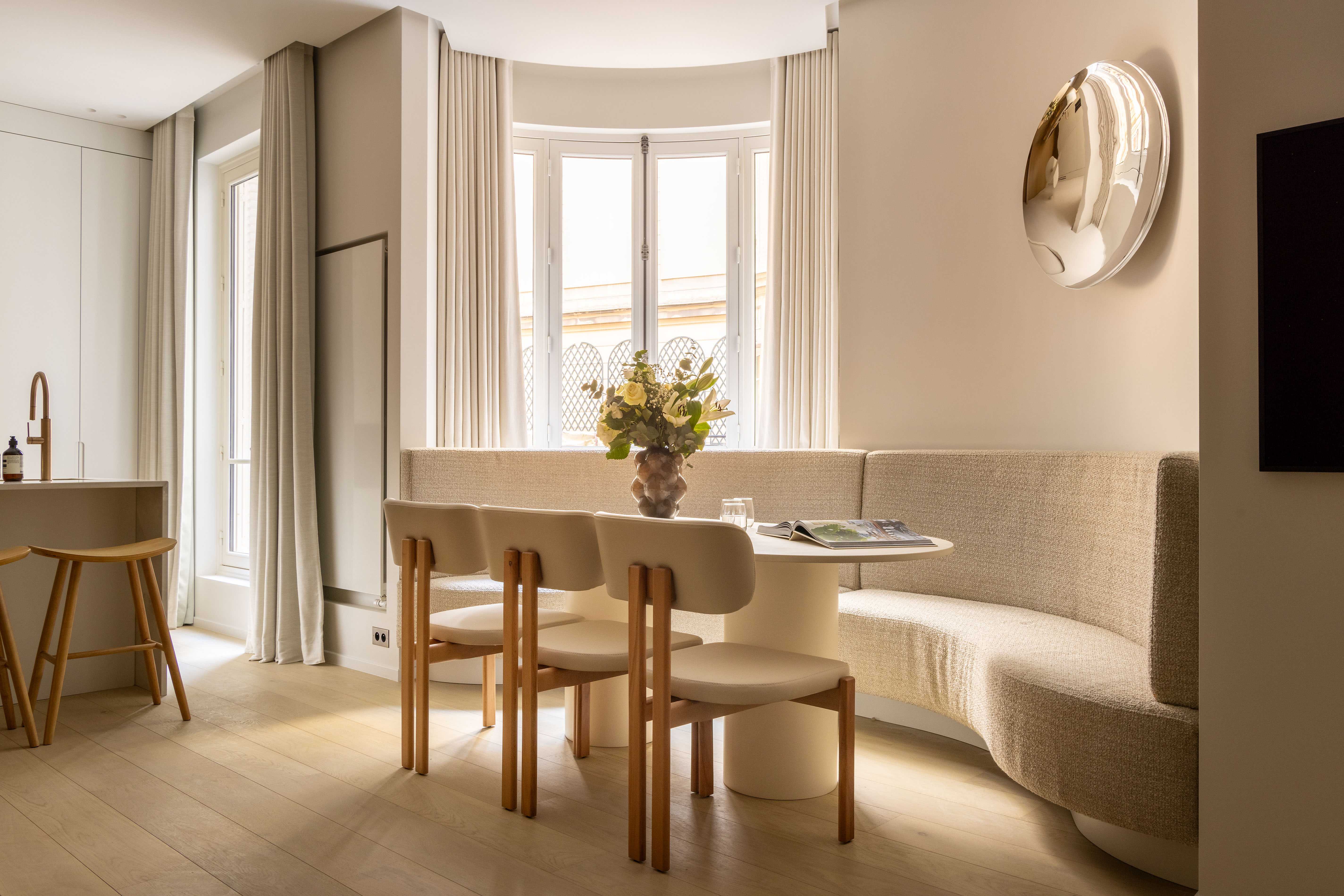 Coin repas avec banquette arrondie, chaises en bois, miroir convexe et fenêtres cintrées