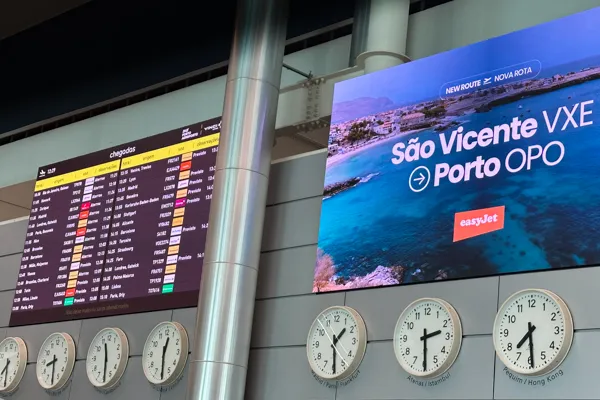 Painel de chegadas e relógios num aeroporto, com voo para o Porto — transferes aeroporto Porto, Vigo e Lisboa · Táxi Afonso · 11 Moledo e Cristelo