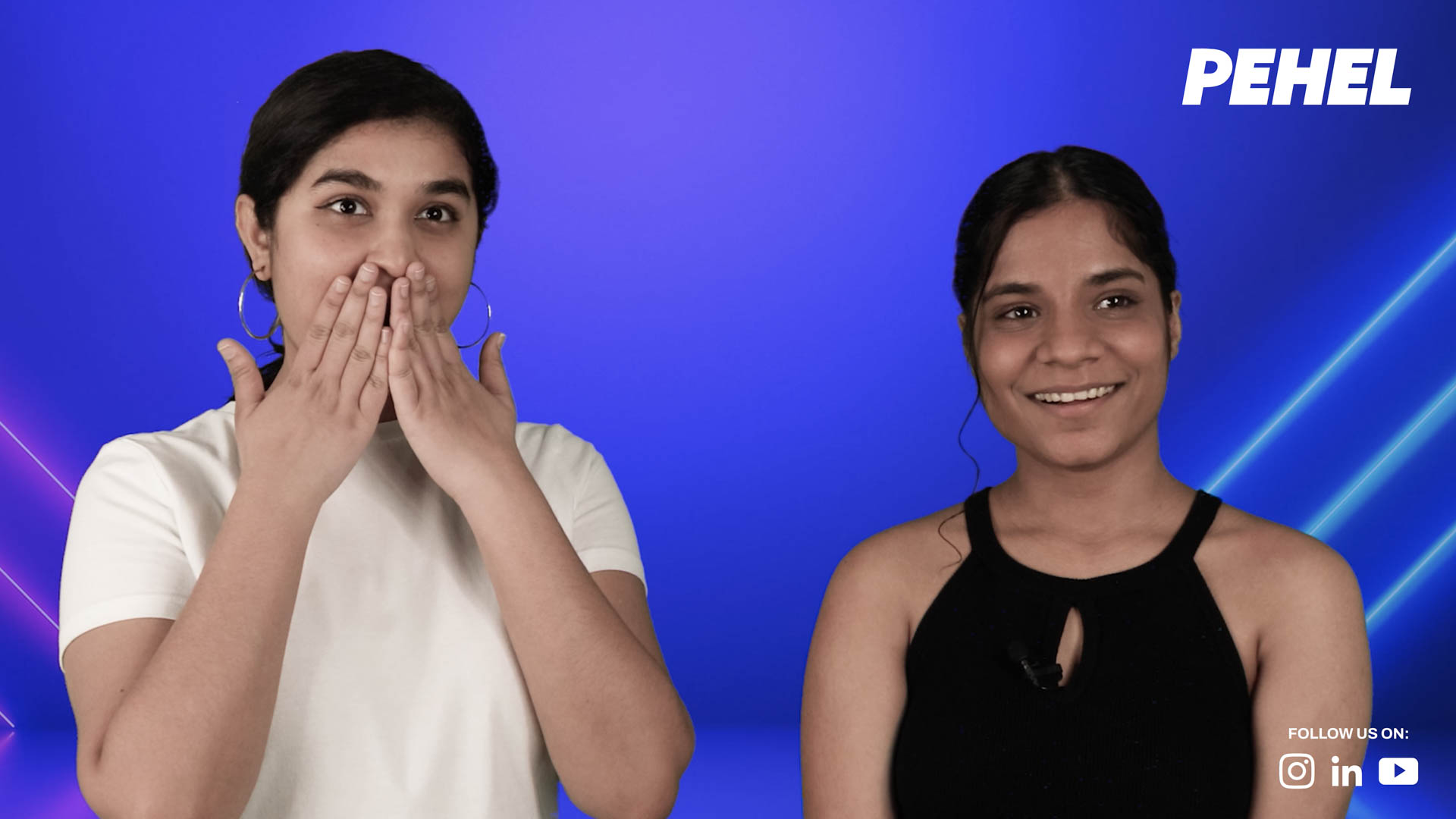 Two women stand side by side against a bright blue background with pink and blue light streaks. The woman on the left wears a white t-shirt and large hoop earrings, her hands covering her mouth. The woman on the right wears a black sleeveless top with a cutout neckline and smiles at the camera. The PEHEL logo appears in the top right corner. Text at the bottom right reads “FOLLOW US: @pehel_instagram_link_icon_videos”.
