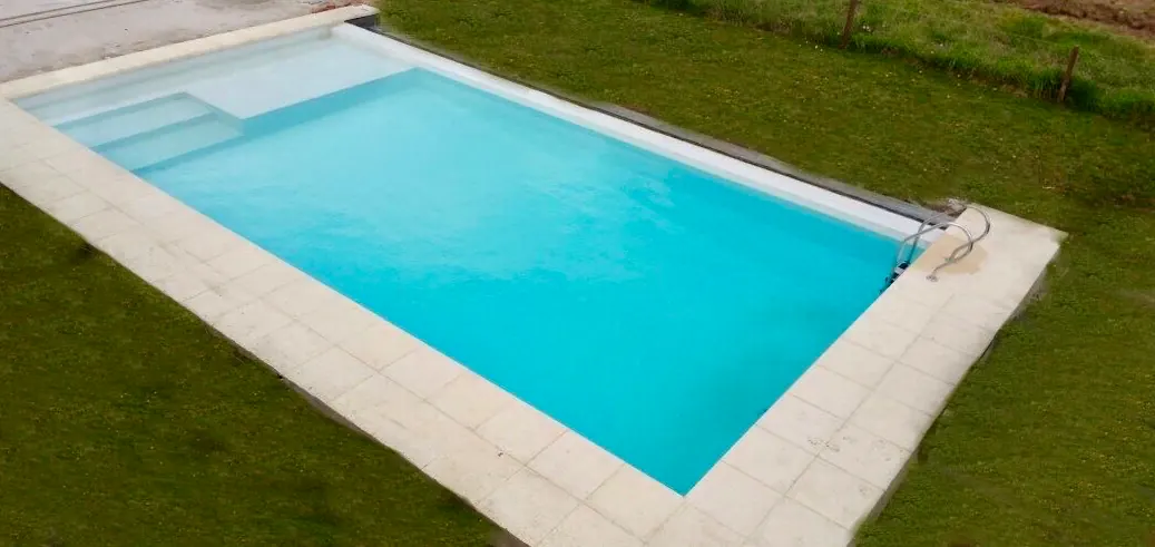 Construcción terminada de piscina clásica de hormigón en un jardín amplio, con escalera de material ancha y revestimiento Aquavations color celeste vibrante.