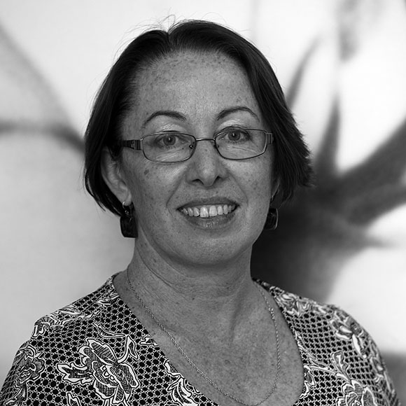 A black-and-white image of Lynne Small, a white woman with short, dark hair and glasses, wearing a floral shirt