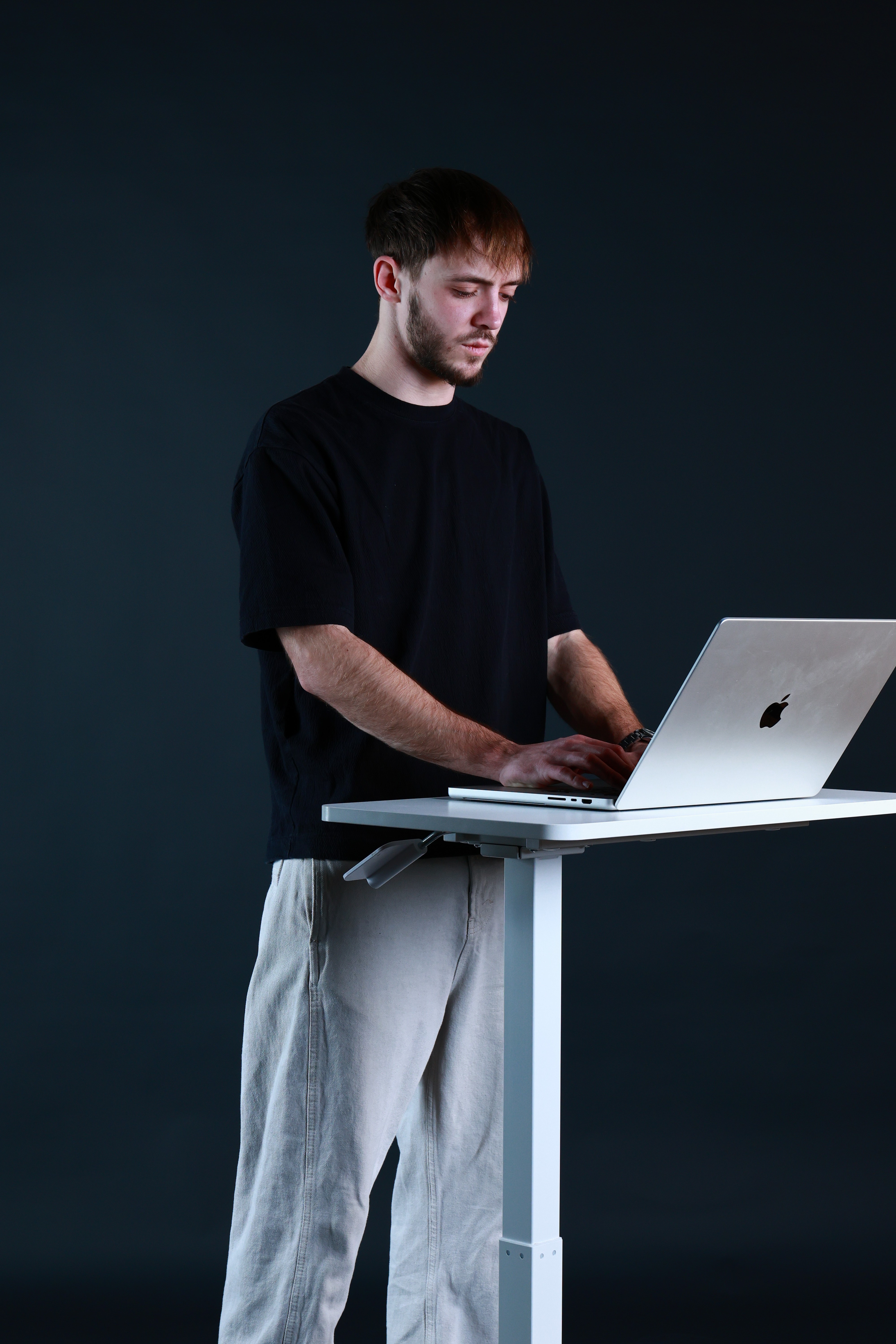 Man sitting in a dimly lit room, wearing a beige shirt and looking contemplative.