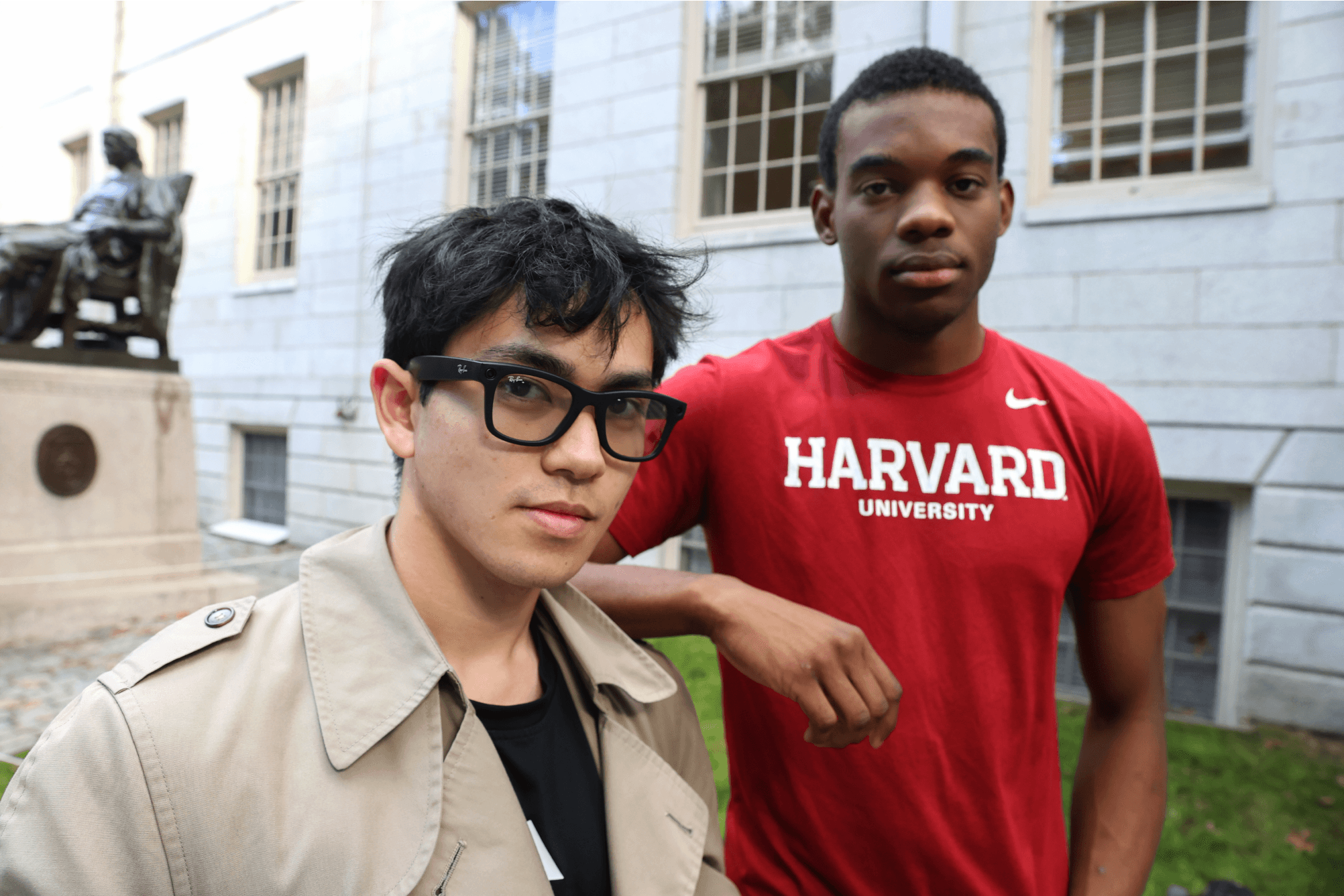 Two students posing for the camera in front of the John Harvard Statue, wearing Meta Ray Bans AI glasses.