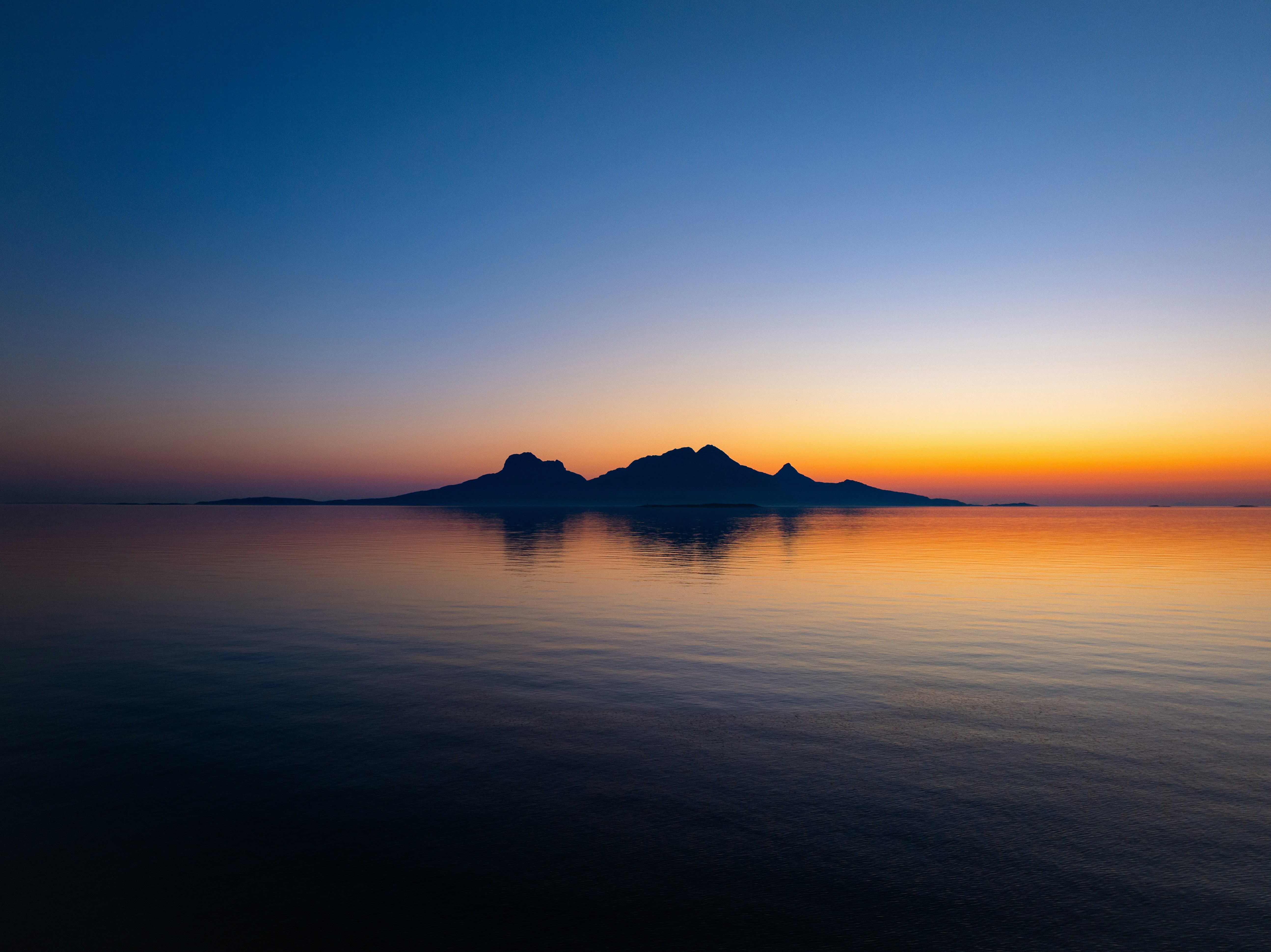 Silhouette of islands on calm ocean at sunset