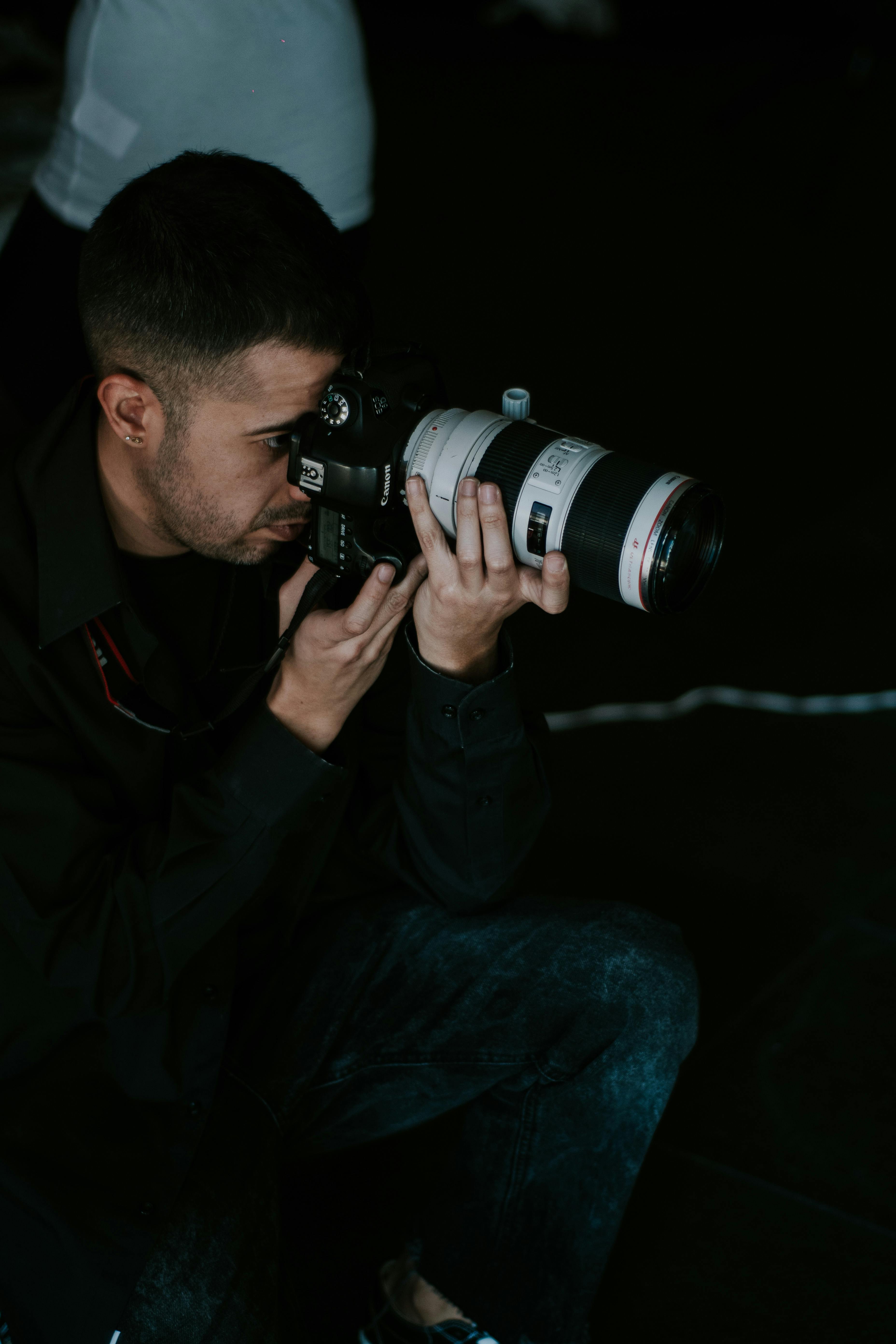 Photographer holding a camera with a large lens in a dark studio